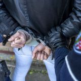 Person von hinten mit blauer Jeans und schwarzer Lederjacke hat die Hände auf dem Rücken und Handschellen an den Handgelenken, links und rechts sind zwei Polizisten in Teilen erkennbar, die die Person festhalten