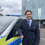 Emir Tarik, der neue Kontaktbeamte, steht lächelnd vor einem Streifenwagen