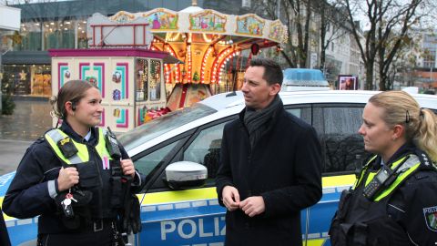 Landrat Andreas Müller spricht mit zwei Polizeibeamtinnen der Mobilen Wache zum Start des Siegener Weihnachtsmarktes 2024